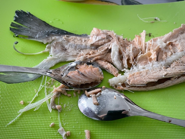 Kypsä kalanruoto leikkuulaudalla, lusikalla irroitetaan kalan lihaa ruodoista